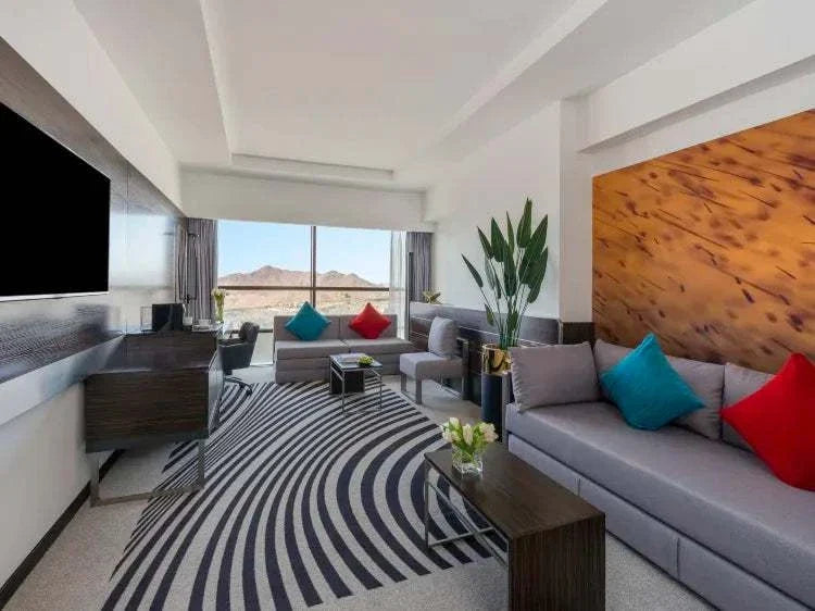 Novotel Makkah Thakher City modern hotel suite with grey sofas, colourful cushions, wood wall and striped rug
