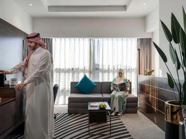 Novotel Makkah Thakher City hotel suite with modern furnishings, grey sofa, teal cushion, and guests