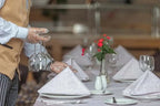 Novotel Makkah Thakher City restaurant table with white patterned napkins, glassware, red flowers, and gloved server