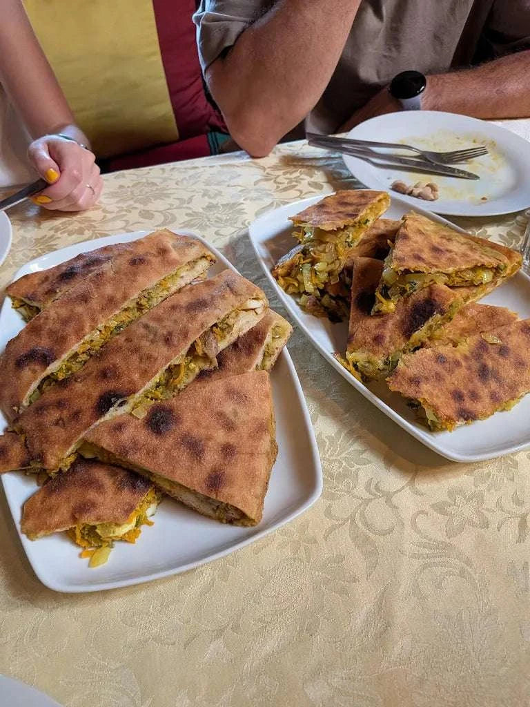 Berber stuffed pizza with a golden-brown crust and vegetable filling served on white plates, Order Pizza option.