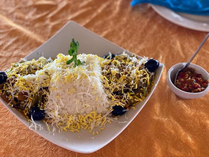 Plate of white rice topped with shredded yellow egg and garnished with a mint leaf, served with a side of vegetable and olive dish and a small bowl of chili pepper to Order Pizza.
