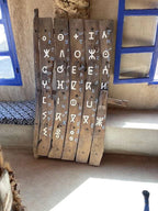 Wooden rustic board with white painted symbols and letters displayed upright beside a window and bench, Order Pizza