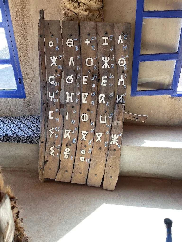 Wooden rustic board with white painted symbols and letters displayed upright beside a window and bench, Order Pizza
