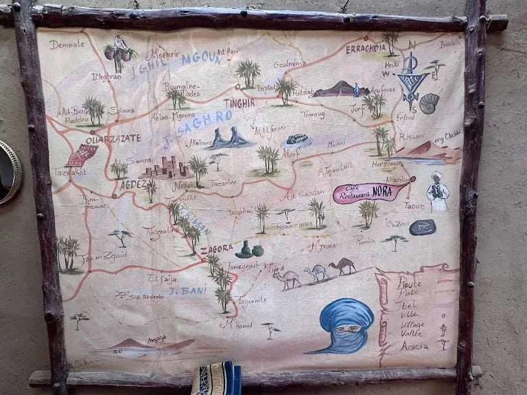 Hand-painted rustic map on parchment paper framed with wooden branches featuring locations and landmarks in Morocco’s Sahara region.