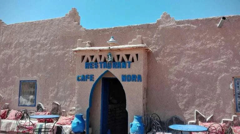 Restaurant building with rustic beige stone walls and blue accents, with outdoor seating, inviting guests to Order Pizza.