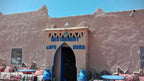 Restaurant building with rustic beige stone walls and blue accents, with outdoor seating, inviting guests to Order Pizza.