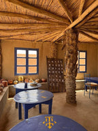 Order Pizza at restaurant seating with blue round tables, wooden roof beams, and beige clay walls featuring traditional decor.