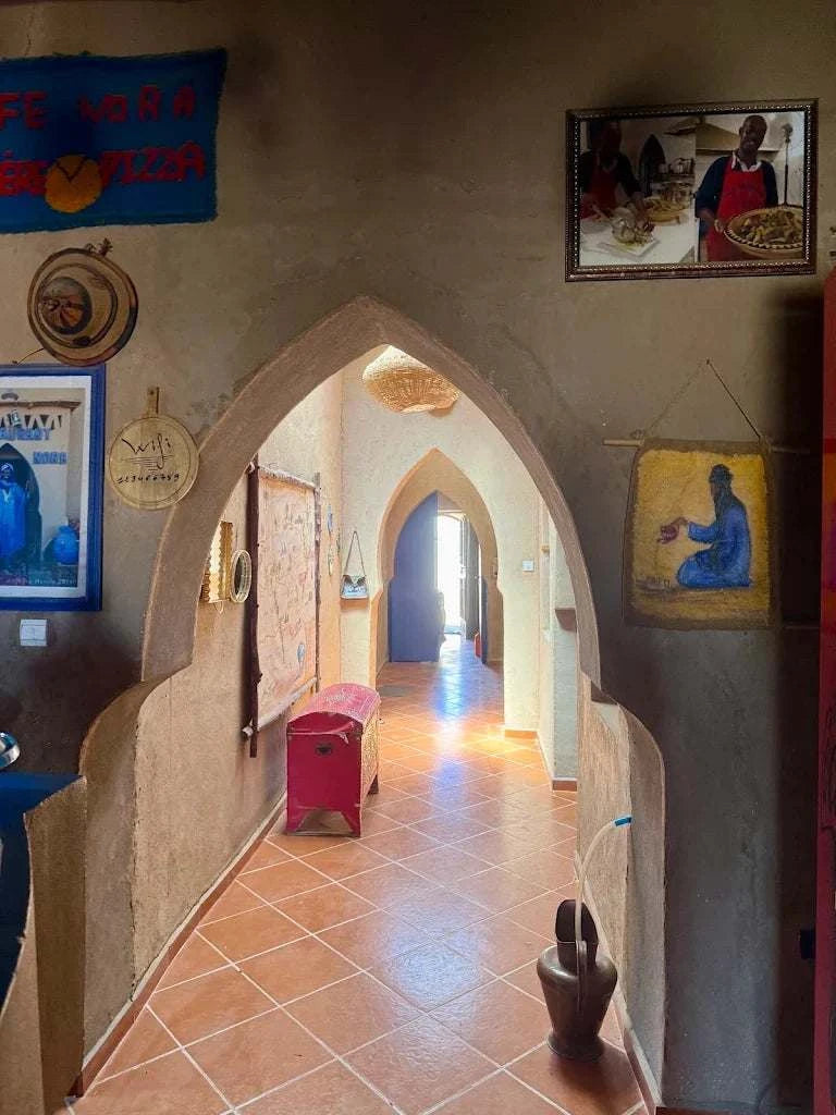 View through a terracotta arched doorway into a tiled hallway with Berber décor, inviting to Order Pizza at Restaurant Nora