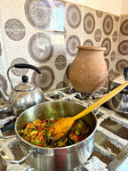 Cooking pot with mixed vegetables and peppers on rustic stove beside metal kettle and clay pot, highlighting the option to Order Pizza.
