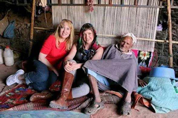 Three people sitting together on colorful patterned rugs inside a rustic tent, illustrating an Overnight Stay with Nomadic People.