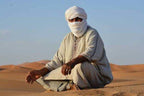 Man dressed in traditional loose light-colored clothing and turban sitting on sand dunes in desert during Overnight Stay with Nomadic People experience