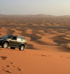 Private Guide for Driving showing a grey 4x4 vehicle navigating soft, golden sand dunes in Erg Chebbi desert at sunset