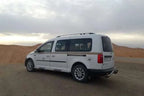 White spacious van with tinted windows and silver rims parked on desert terrain, ideal for Private Taxi from Erfoud to Merzouga.