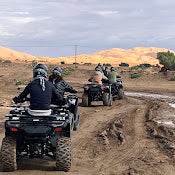 quad bike ride with riders on black all-terrain vehicles on dirt path with golden desert dunes in the background