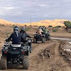 quad bike ride with riders on black all-terrain vehicles on dirt path with golden desert dunes in the background