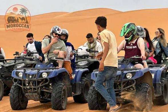 Group of people on blue all-terrain quad bikes with helmets on sandy Merzouga dunes during a quad bike ride adventure.