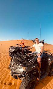 quad bike ride with two people on black all-terrain vehicles on orange desert sand under clear blue sky