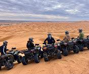 quad bike ride across sandy golden dunes with riders wearing helmets and gear lined up on black quad bikes under a cloudy sky