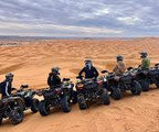 quad bike ride across sandy golden dunes with riders wearing helmets and gear lined up on black quad bikes under a cloudy sky
