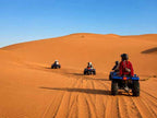 quad bike ride across golden orange sand dunes with riders wearing helmets and protective gear under clear blue sky