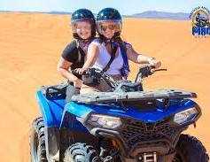 quad bike ride featuring two riders on a blue all-terrain vehicle with helmets, set on golden desert dunes