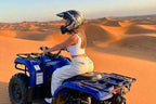 Woman wearing a helmet on a blue quad bike in beige pants and white top with orange sand dunes in the background during quad bike ride