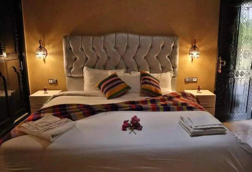 Residence Touristique Merzouga bedroom with beige tufted headboard, white bedding, colorful striped pillows and throw, and wall sconces
