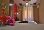 Residence Touristique Merzouga bedroom with soft beige walls, warm lighting, decorative brass and red vase, and pink flowers on textured fabric surface