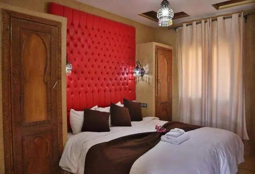 Residence Touristique Merzouga bedroom featuring red tufted headboard, white bedding with brown runner and pillows, rustic carved wooden doors