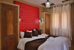 Residence Touristique Merzouga bedroom featuring red tufted headboard, white bedding with brown runner and pillows, rustic carved wooden doors