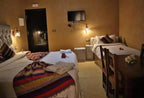Residence Touristique Merzouga cozy bedroom with beige walls, two beds featuring colorful striped throws and pillows, wooden chairs, and soft lighting