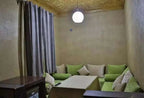 Residence Touristique Merzouga living room with beige textured walls, green and beige cushions, gold ornate ceiling, and grey curtains