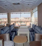 Residence Touristique Merzouga lounge area with plush blue velvet sofas, beige armchairs, white tables, and large windows overlooking desert landscape