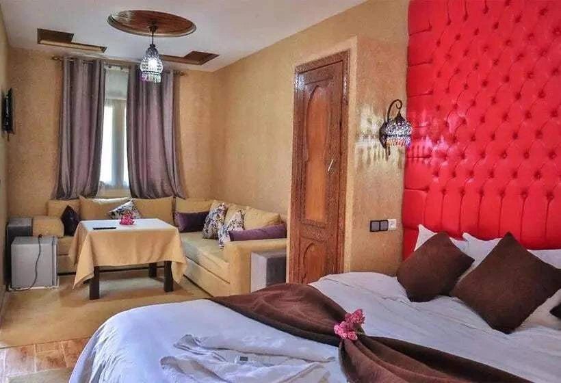 Residence Touristique Merzouga room featuring a red tufted headboard, white and brown bedding, beige walls, and a cozy beige sofa with a small table