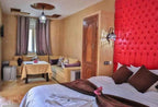 Residence Touristique Merzouga room featuring a red tufted headboard, white and brown bedding, beige walls, and a cozy beige sofa with a small table