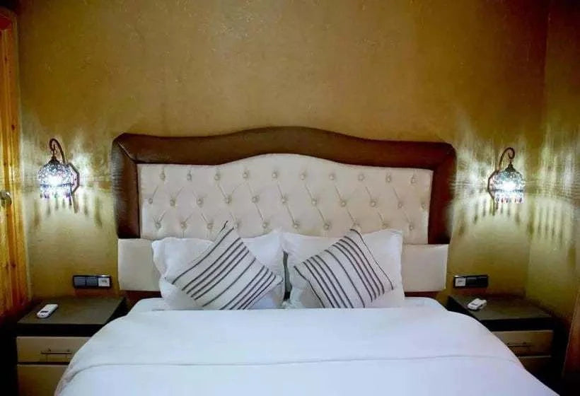 Residence Touristique Merzouga room with large bed, tufted headboard, striped pillows, wooden side tables, and ornate wall lamps
