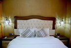 Residence Touristique Merzouga room with large bed, tufted headboard, striped pillows, wooden side tables, and ornate wall lamps