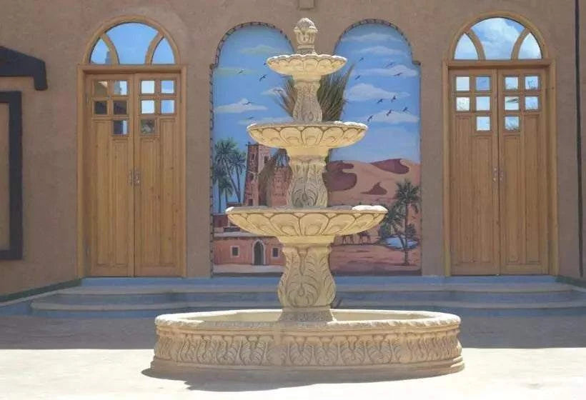 Residence Touristique Merzouga beige decorative stone fountain with three tiers in courtyard with wooden doors and desert mural