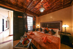 Riad Africa Marrakech bedroom with carved wooden ceiling, dark wood furniture, orange bedspread and pillows, and side lamps