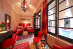 Riad Africa Marrakech bedroom with red velvet chairs, twin beds with red bedding, patterned rug, and window view of pool
