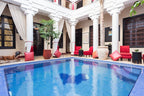 Riad Africa Marrakech courtyard with blue tiled swimming pool, white columns, beige walls, red cushioned chairs, and decorative plants