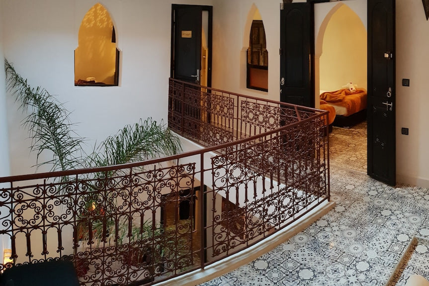 Riad Africa Marrakech interior featuring intricate brown wrought iron railings, patterned tiled floor, white walls, and warmly lit archways.