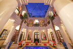 Riad Africa Marrakech courtyard with beige columns, blue pool, red cushions, tall windows, and evening sky