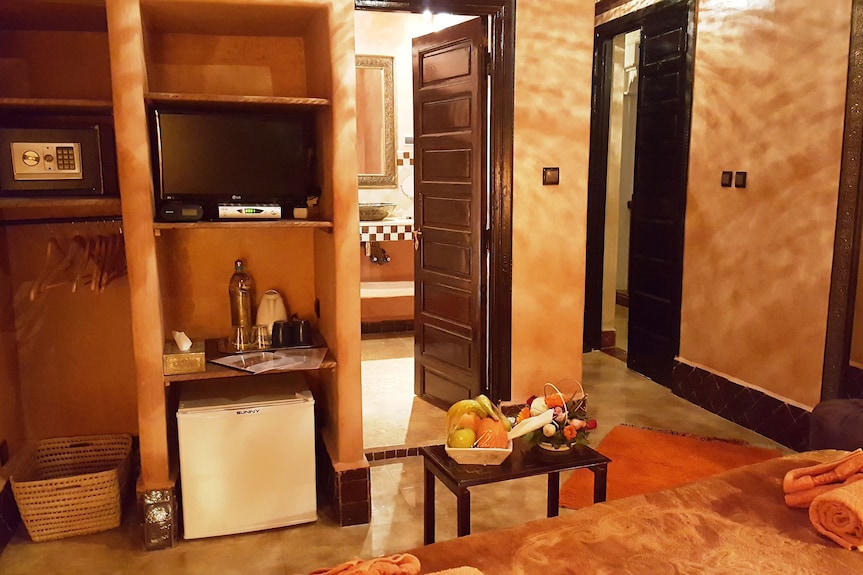 Riad Africa Marrakech cozy room with warm earthy tones, wooden doors, small fridge, TV, safe, and a table with fresh fruit basket