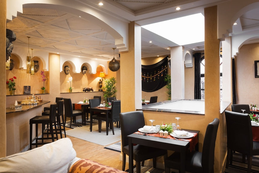 Riad Africa Marrakech dining area with warm-toned walls, black leather chairs, wooden tables, and decorative African masks