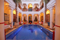Riad Africa Marrakech featuring an indoor blue pool surrounded by white columns, red accents, and draped curtains in a traditional Moroccan courtyard