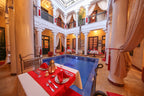 Riad Africa Marrakech indoor courtyard with blue tiled pool, yellow ochre walls, white columns, and red table settings