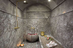 Riad Africa Marrakech traditional Moroccan hammam with grey marble walls, brass fixtures, stone basin with rose petals, and leopard print massage table