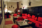 Riad Africa Marrakech lounge with red cushioned seating, black wood paneling, Moroccan decorative masks, and a traditional fireplace