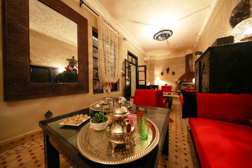 Riad Africa Marrakech elegant lounge with red cushioned seating, traditional silver tea set on glass table, and Moroccan decor